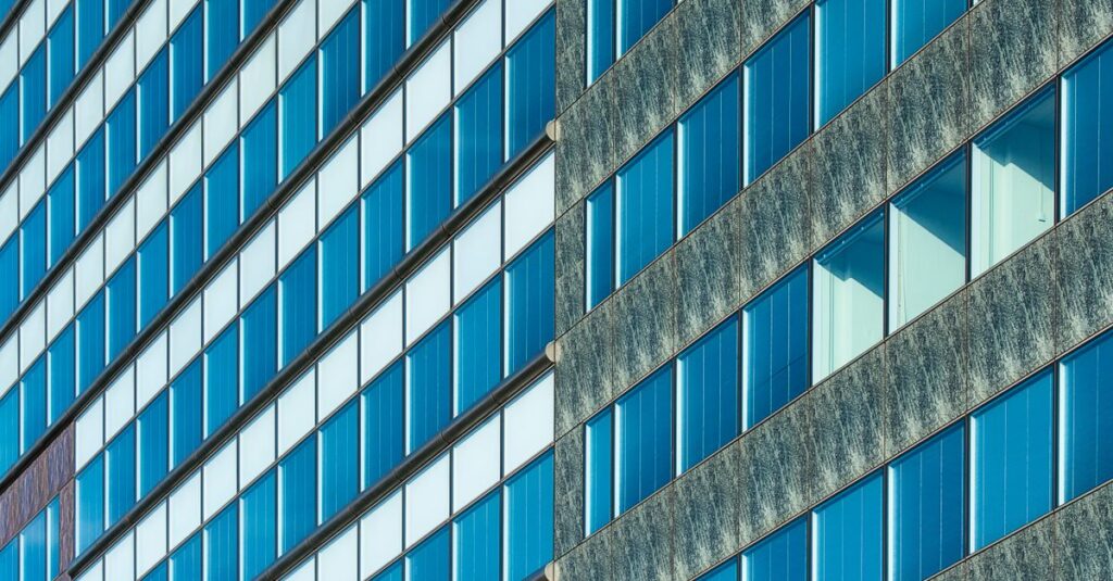 Close-up of a modern glass facade with diagonal lines and windows reflecting blue hues.