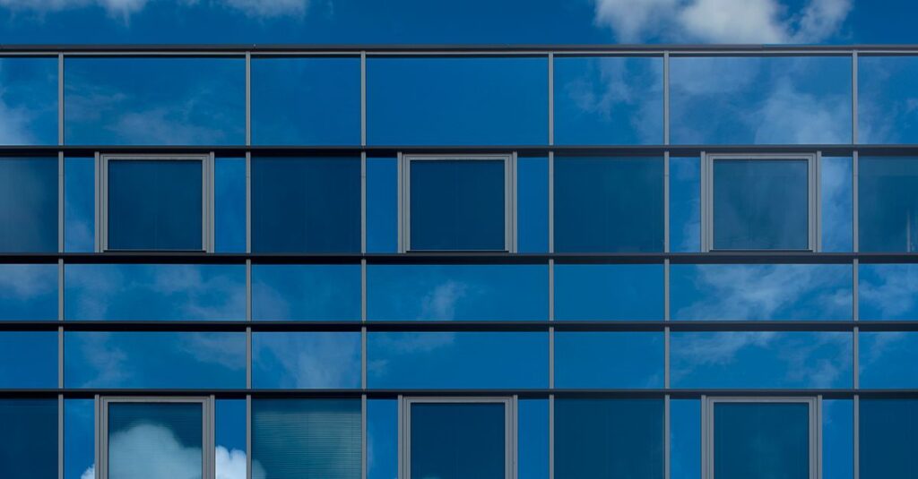 Facade of a modern glass building reflecting the blue sky and clouds.