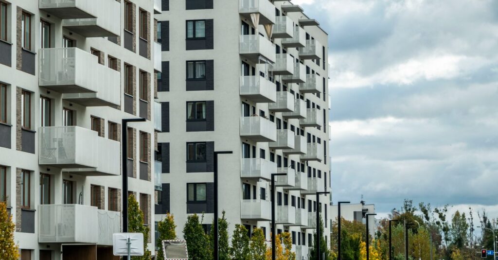 Contemporary apartment complex on a city street lined with parked cars and autumn foliage.