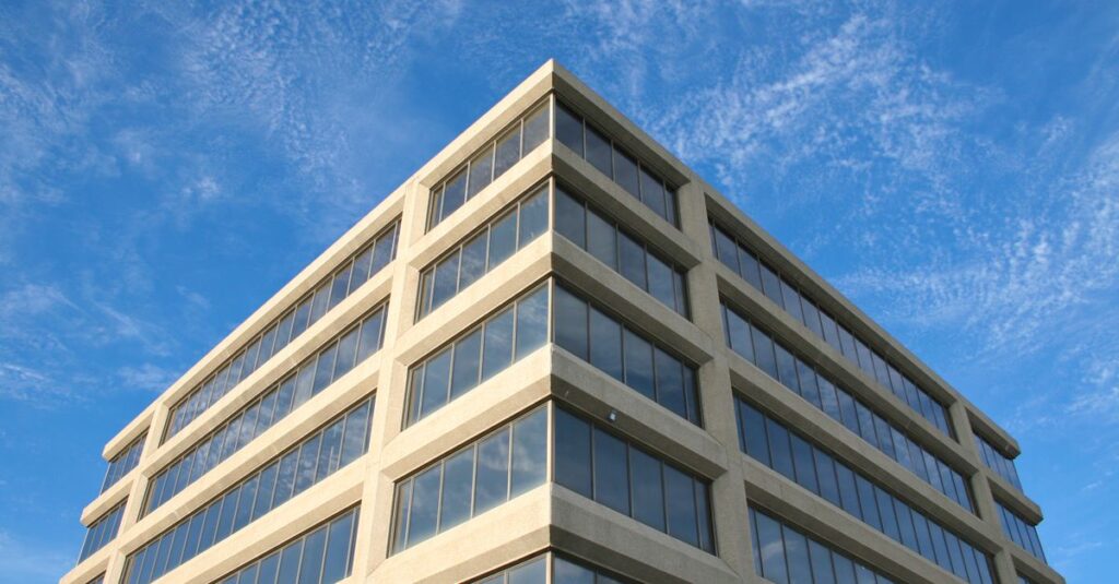 Corner view of a modern office building with reflective windows under a clear blue sky.